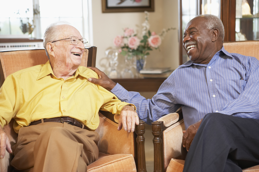 Senior men relaxing in armchairs at their retirement community and sharing a laugh while they socialize together